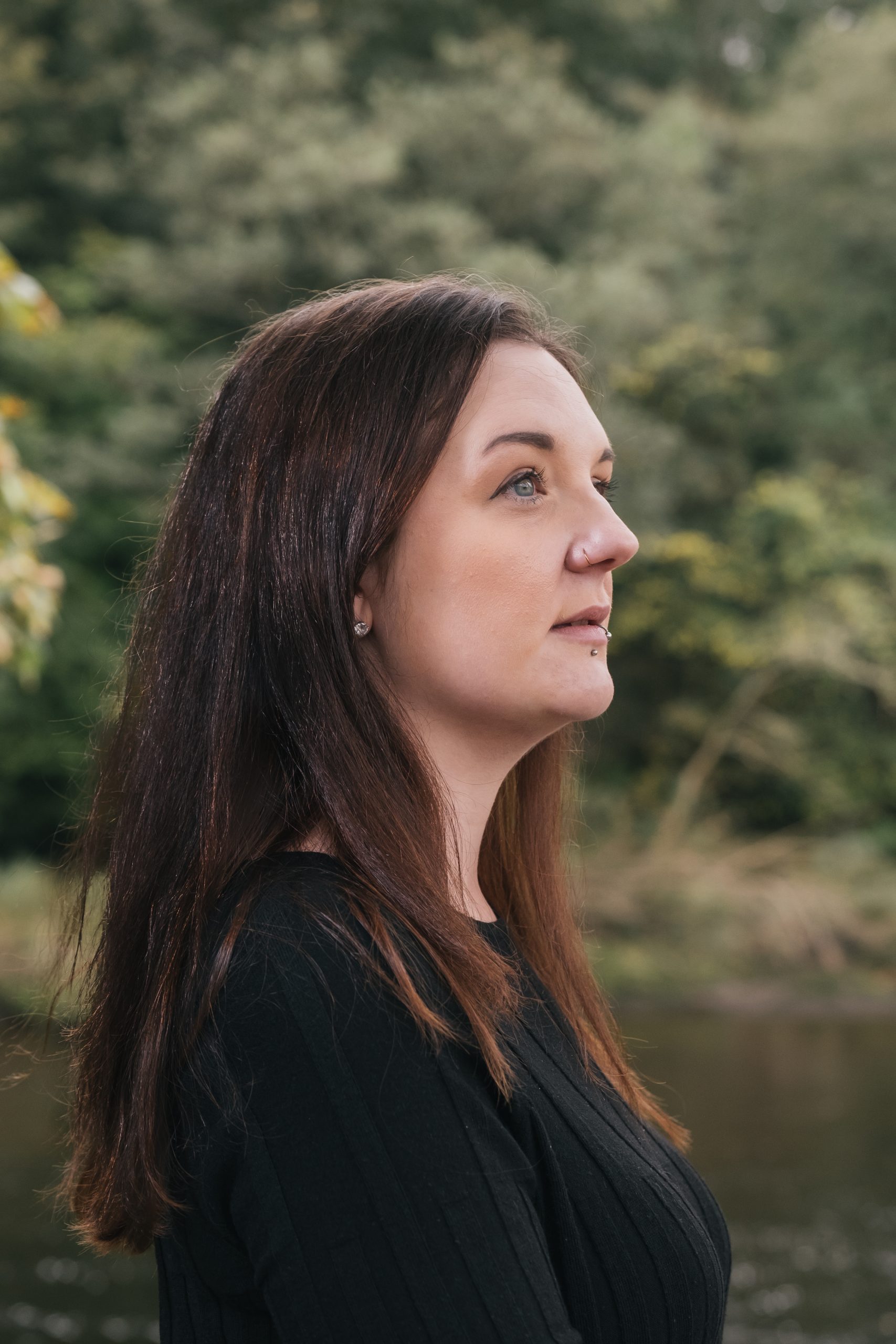 Sarah Hutt standing outdoors in profile, looking out to the side, with green trees in the background