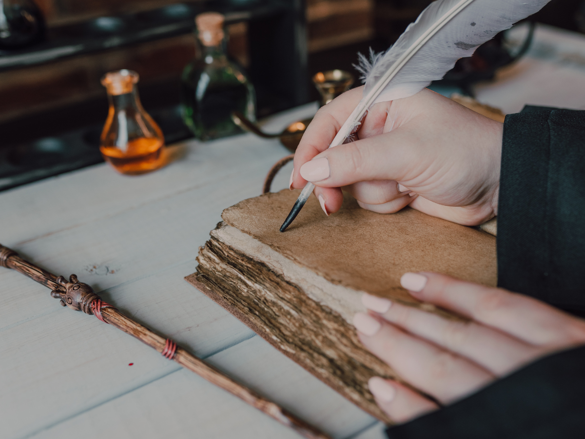 A hand writing with a feather quill pen in an old leather-bound notebook, with glass ink bottles nearby